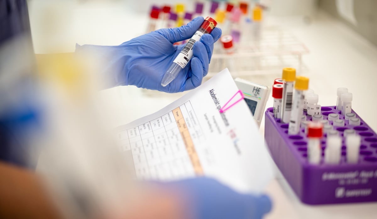 En person i blå handskar håller i ett provrör.